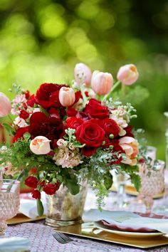 a vase filled with red and pink flowers sitting on top of a table next to silverware