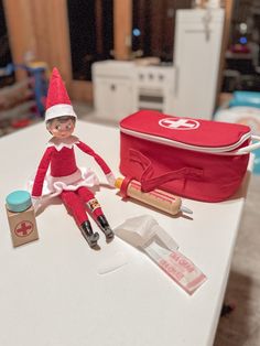 an elf sitting on top of a table next to a red bag and other items