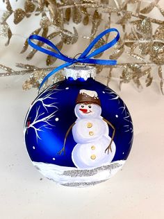 a glass ornament with a snowman painted on it's side and blue ribbon