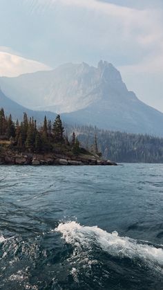 an island in the middle of water with trees on it and mountains in the background