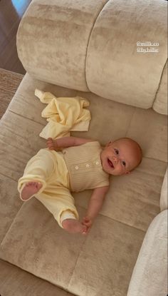 a baby laying on top of a couch next to a remote control