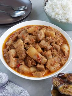 a white bowl filled with meat and rice next to a plate of food on a table