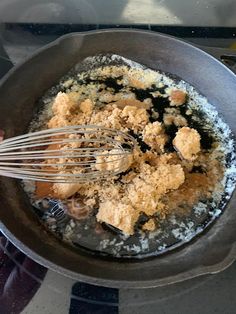 a pan filled with food on top of a stove next to a person holding a whisk