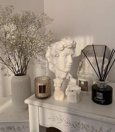 a white mantle topped with vases filled with flowers and candles next to a statue