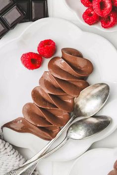 a white plate topped with chocolate and raspberries next to two silver spoons