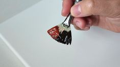 a hand holding a paintbrush with red and black brush on it's tip