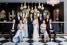 a group of people standing and sitting in front of a bar with chandeliers