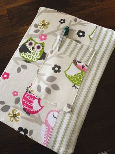 an ipad case is decorated with owls and flowers on white fabric, sitting on a wooden table