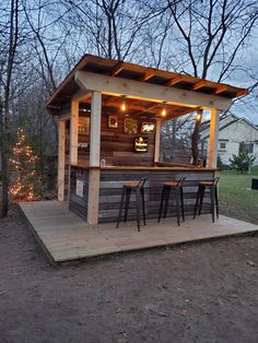 an outdoor bar with three stools and lights on the outside, next to some trees