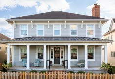 a large gray house with white trim on the front door and porch, along with two blue chairs