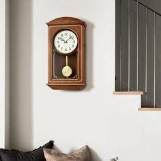 a clock mounted to the side of a wall next to a stair case in a living room