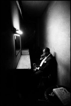 a man sitting in a dark room next to a wall with a light on it