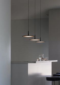 three lights hanging over a bar with wine glasses on the counter and two stools