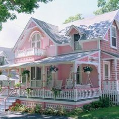 a pink house with white trim on the front porch and two story windows, covered in flowers