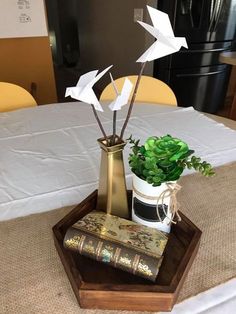 a vase with some plants in it sitting on a wooden tray next to a book