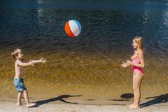 two young children playing with a beach ball on the shore of a body of water