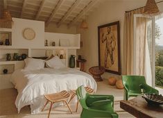 a bedroom with a large bed and green chairs in front of a window that looks out onto the countryside