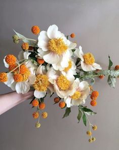 a hand holding a bouquet of flowers with orange and white blooms on it's stems