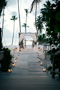 an outdoor wedding set up on the beach with candles and lanterns in front of it