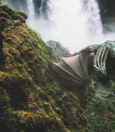 a dragon sculpture sitting on top of a lush green hillside next to a waterfall in the background