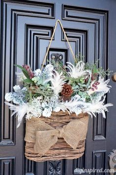 a basket filled with white flowers and greenery hanging from a door handle on a black front door