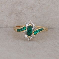 an emerald and white diamond ring on a stone surface with two diamonds in the middle