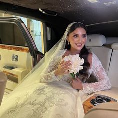 a bride sitting in the back of a car with flowers on her lap and smiling at the camera