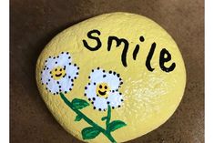 a painted rock with flowers and the words smile on it