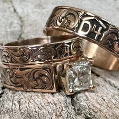 two wedding rings with an engraved design and a princess cut diamond on the side, sitting on a rock