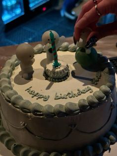 someone is lighting candles on a birthday cake with white frosting and green icing