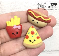 three miniature food items in the palm of someone's hand, one with a hot dog and fries on it