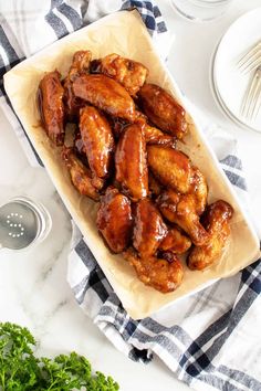 chicken wings on a plate with sauce and parsley next to the bowl full of them