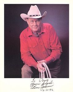 an old man in a red shirt and cowboy hat holding a white rope with his right hand