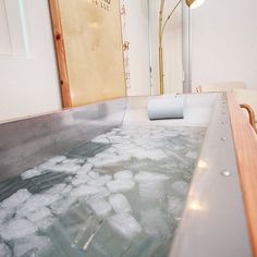 a bathtub filled with ice and water next to a wooden table in a room