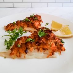 a white plate topped with fish covered in sauce and garnish