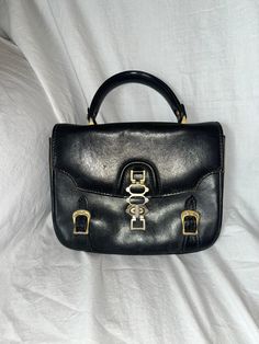 "Gorgeous vintage handbag that is in need of a little TLC, circa probably 1970s. Front closure has three toggle \"lengths\" and there are two faux buckle details. The exterior leather could use a shining up, but otherwise is in pretty good condition. The interior, sadly, has quite a bit of pen marking inside, but is in functionally great shape. Interior zip pocket still opens smoothly and is clean - please see photographs for item you will receive. For high quality vintage fashion at an affordab Vintage Satchel With Metal Hardware, Vintage Shoulder Bag With Metal Hardware, Vintage Shoulder Bag With Metal Hardware For Daily Use, Vintage Leather Bags With Metal Hardware, Vintage Bags With Metal Hardware For Daily Use, Retro Shoulder Bag With Metal Hardware, Vintage Formal Satchel With Metal Hardware, Vintage Rectangular Bag With Metal Hardware, Retro Satchel With Metal Hardware