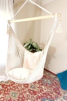 a white hammock hanging from a ceiling in a room with a rug and potted plant