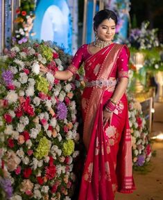 a woman in a red sari standing next to flowers