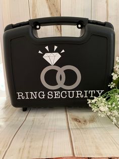 a black case with two wedding rings on it and a flower in the corner next to it