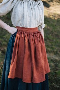 a woman standing in the grass with her hands on her hips and wearing a skirt