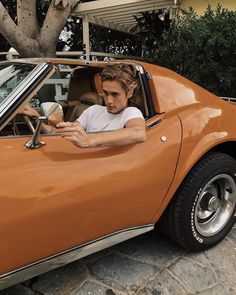 a man sitting in the driver's seat of an orange sports car