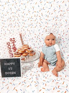 a baby sitting in front of a table with doughnuts and a happy birthday sign