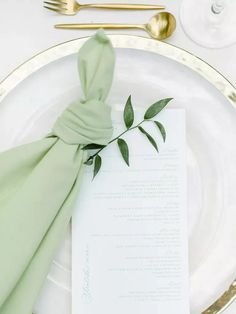 a place setting with green napkins and gold cutlery on a white plate,