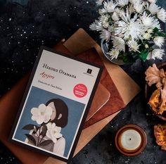 an open book sitting on top of a table next to some flowers and a candle