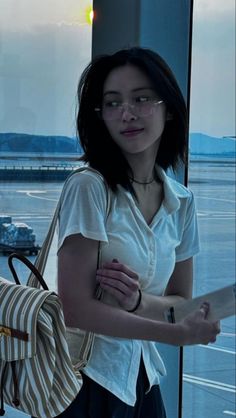 a woman standing in front of a window with a handbag on her shoulder and looking at the camera