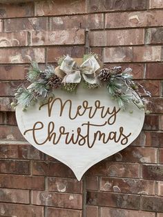 a merry christmas sign hanging on the side of a brick building with pine cones and greenery