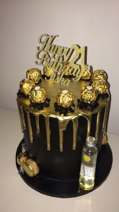 a black and gold birthday cake on a white table with a bottle of liquor next to it