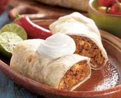 two burritos on a plate with sour cream in the middle and some vegetables