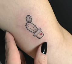 a woman's hand with a small cactus tattoo on her left arm, and a tiny red heart in the middle