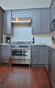 a kitchen with gray cabinets and stainless steel appliances in the center, along with hardwood floors